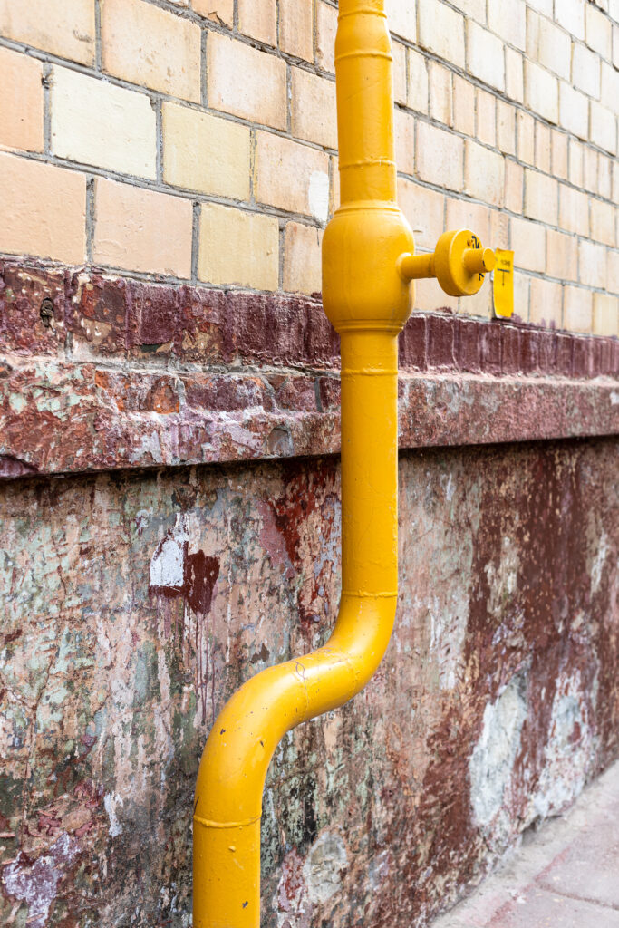 Yellow pipe running along a brick wall