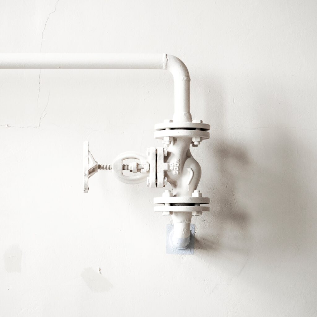 White-painted pipework with a valve on a white wall